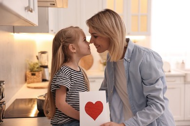 Photo of Little daughter congratulating her mom with greeting card in kitchen. Happy Mother's Day