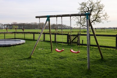 Photo of Wooden swings and trampoline on green lawn outdoors