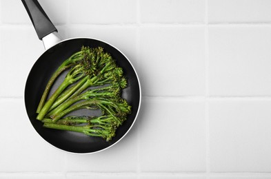 Photo of Frying pan with tasty cooked broccolini on white tiled table, top view. Space for text