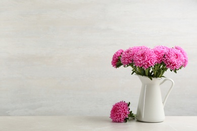 Photo of Beautiful pink asters in jug on table against white background, space for text. Autumn flowers