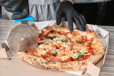 Photo of Professional chef cutting Italian oven baked pizza on table in restaurant, closeup