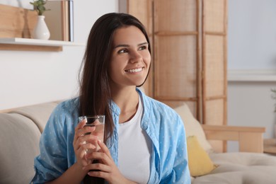 Photo of Happy young woman with glass of water indoors. Refreshing drink