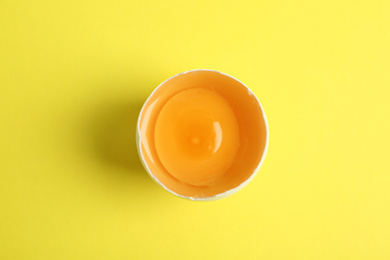 Photo of Broken raw chicken egg on yellow background, top view