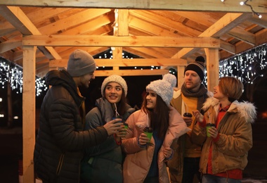 Photo of Happy friends with cups of mulled wine at winter fair