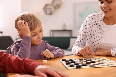 Photo of Family playing checkers at wooden table in room