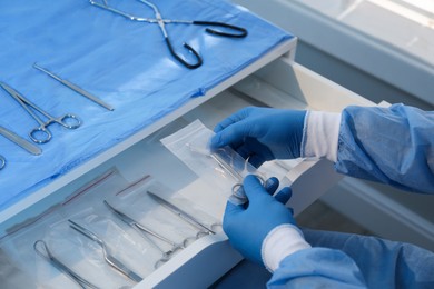 Photo of Doctor putting Pott's scissors into drawer indoors, closeup. Table with different surgical instruments