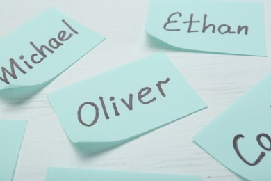 Photo of Paper stickers with different names on white wooden table, closeup. Choosing baby's name