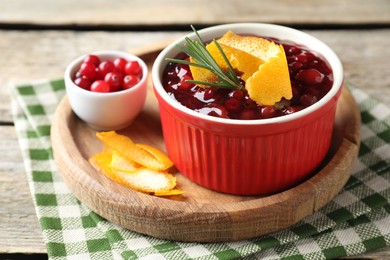 Photo of Cranberry sauce in bowl, fresh berries, rosemary and orange peels on table, closeup