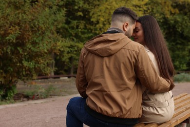 Photo of Young couple spending time together on wooden bench in autumn park, back view. Space for text