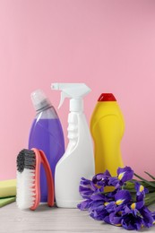 Different cleaning supplies and beautiful spring flowers on white wooden table against light pink background