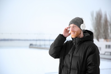 Photo of Young man listening to music with headphones outdoors. Space for text