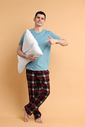 Photo of Happy man in pyjama holding pillow on beige background