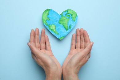 Photo of Woman with heart shaped model of planet on light blue background, top view. Earth Day