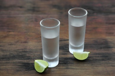 Photo of Mexican tequila shots with lime slices on wooden table. Drink made from agave