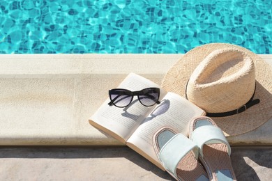 Photo of Stylish sunglasses, slippers, straw hat and book at poolside on sunny day. Beach accessories