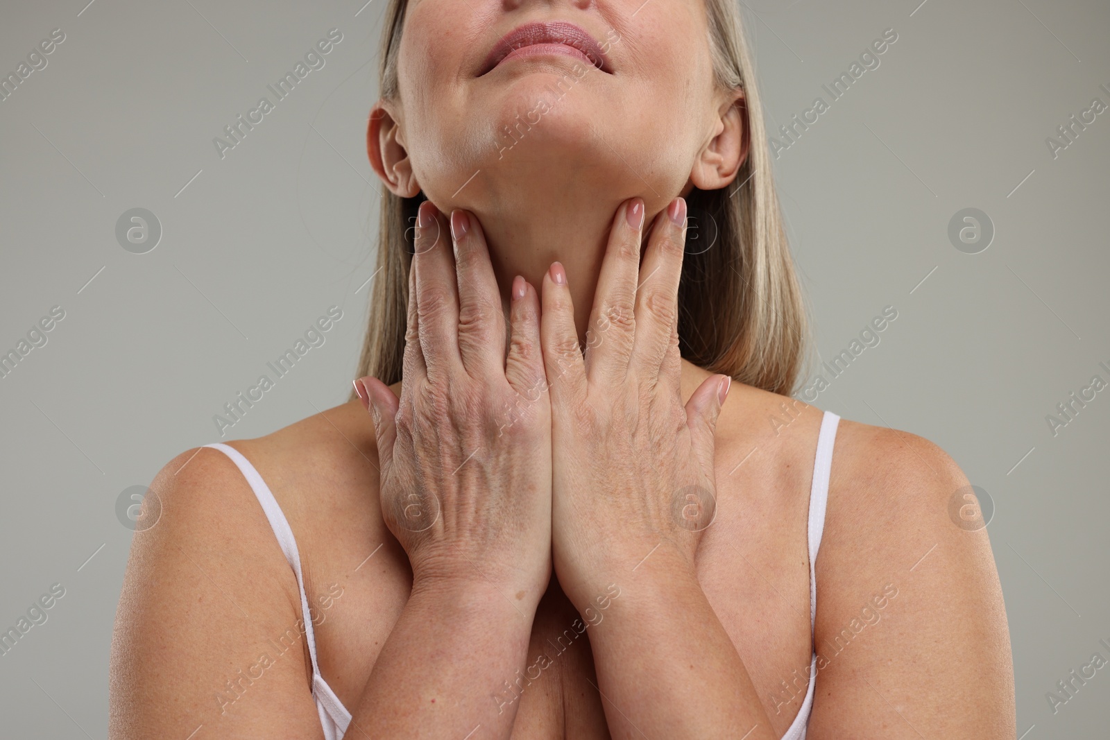 Photo of Mature woman touching her neck on grey background, closeup