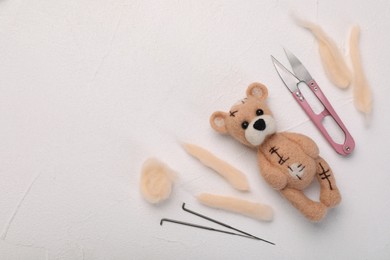 Photo of Felted bear, wool, and tools on white table, flat lay. Space for text