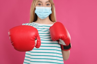 Photo of Woman with protective mask and boxing gloves on pink background. Strong immunity concept