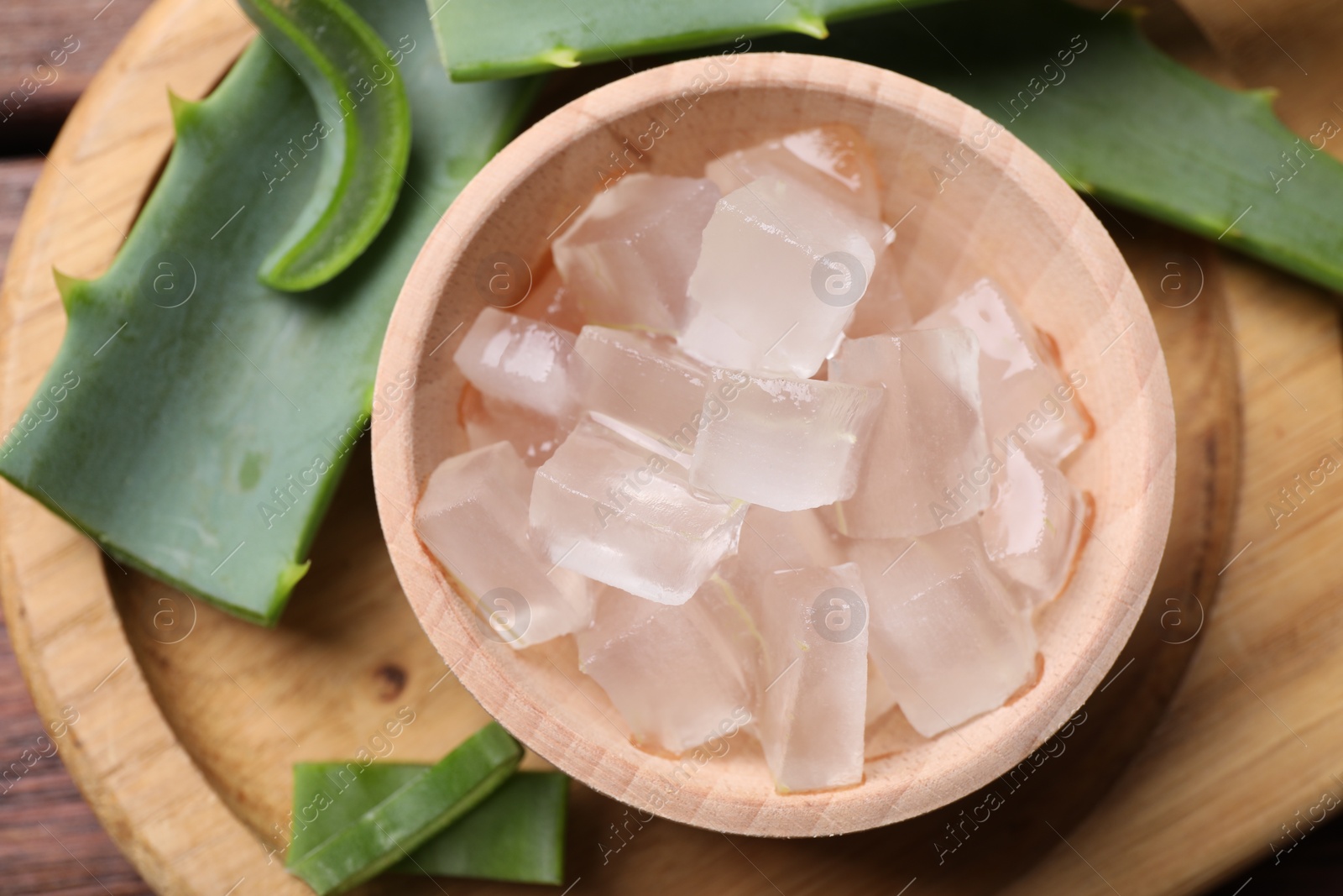 Photo of Aloe vera gel and slices of plant on wooden table, flat lay