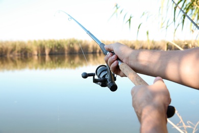 Photo of Man fishing alone at riverside on sunny day, closeup