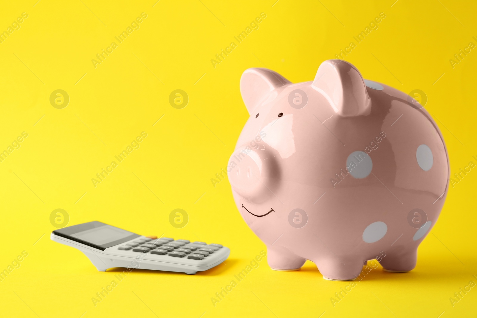 Photo of Calculator and pink piggy bank on yellow background