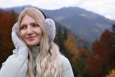 Photo of Young beautiful woman wearing warm earmuffs in mountains