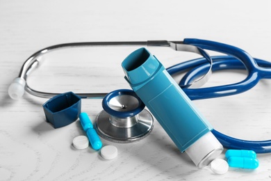 Asthma inhaler, stethoscope and pills on white wooden background