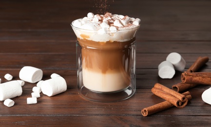 Photo of Glass with delicious coffee drink, marshmallows and cinnamon sticks on wooden table