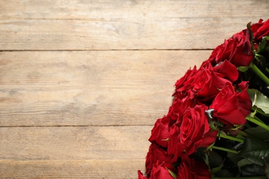 Photo of Luxury bouquet of fresh red roses on wooden table, top view. Space for text