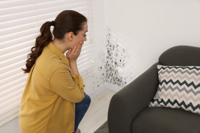 Image of Shocked woman looking at affected with mold walls in room