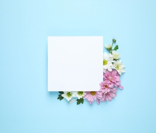 Photo of Beautiful chamomile flowers and paper card on light blue background, flat lay with space for text