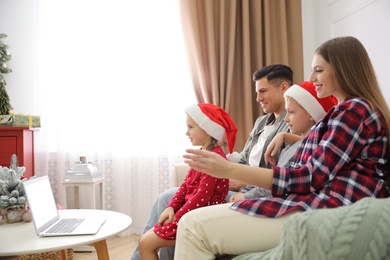 Photo of Family with children using video chat on laptop in room decorated for Christmas