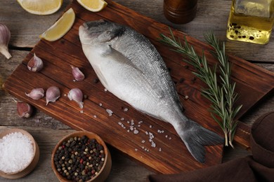 Photo of Raw dorado fish, lemon wedges and spices on wooden table