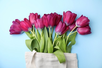 Photo of Beautiful purple tulips in tote bag on light blue background, top view