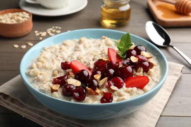 Photo of Bowl of oatmeal porridge served with berries on wooden table, closeup