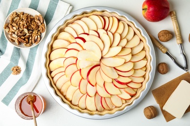Photo of Raw traditional English apple pie in baking dish and ingredients on white table, flat lay