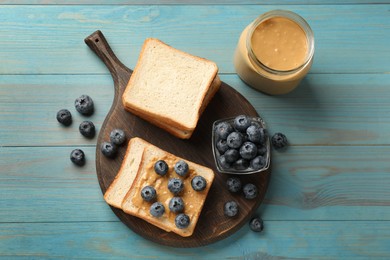 Photo of Delicious toasts with peanut butter and blueberries on light blue wooden table, top view