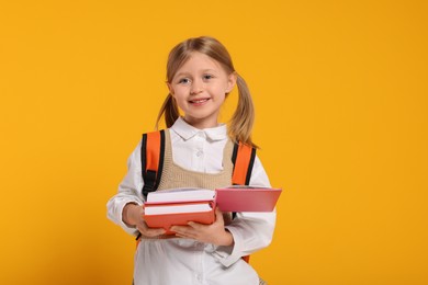 Photo of Happy schoolgirl with backpack and books on orange background