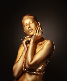Photo of Portrait of beautiful lady with gold paint on skin against black background