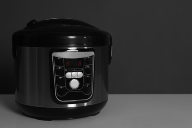 Photo of Modern electric multi cooker on table against dark background. Space for text