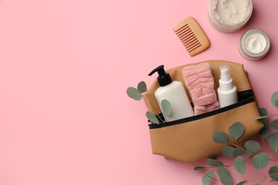 Photo of Preparation for spa. Compact toiletry bag with different cosmetic products, comb and eucalyptus on pink background, flat lay. Space for text