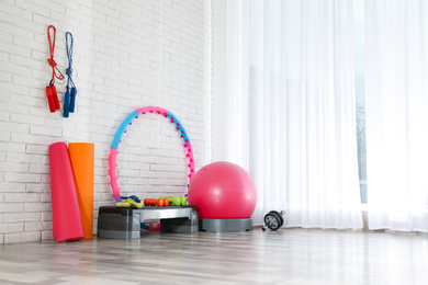 Photo of Different sports equipment near white brick wall in gym. Space for text