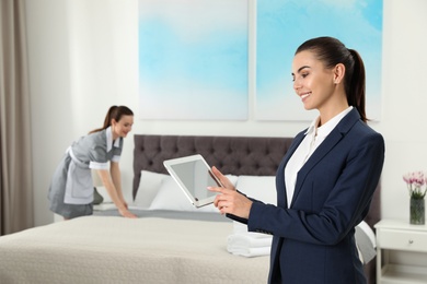 Photo of Housekeeping manager with tablet checking maid work in hotel room. Space for text
