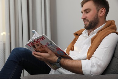 Photo of Handsome man reading magazine in armchair indoors