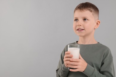 Photo of Cute boy with glass of fresh milk on light grey background, space for text