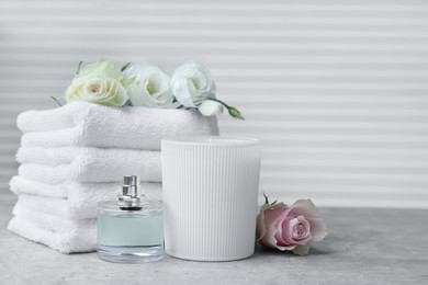 Photo of Towels, bottle of perfume, scented candle and flowers on grey table indoors