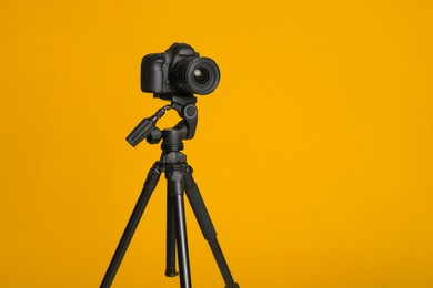 Photo of Modern tripod with professional camera on yellow background. Space for text