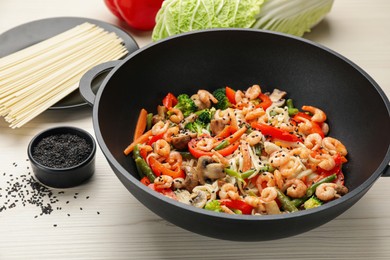 Stir fried noodles with mushrooms, shrimps and vegetables in wok on white wooden table