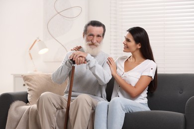 Photo of Senior man with walking cane and young woman on sofa at home
