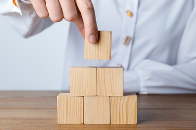 Photo of Woman building pyramid of cubes on wooden table, closeup. Space for text